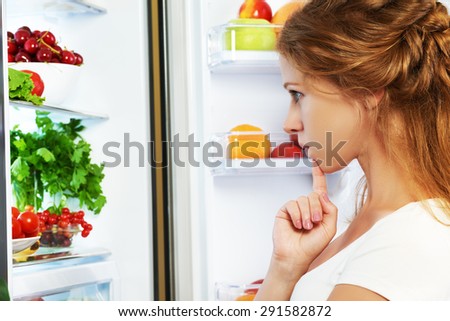 Happy woman standing at the open refrigerator with fruits, vegetables and healthy food