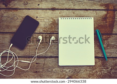 cell phone, headphones, notebook and pen on the old wooden table