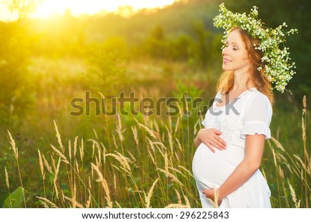 beautiful pregnant woman in wreath  relaxing in the summer nature meadow with sunset