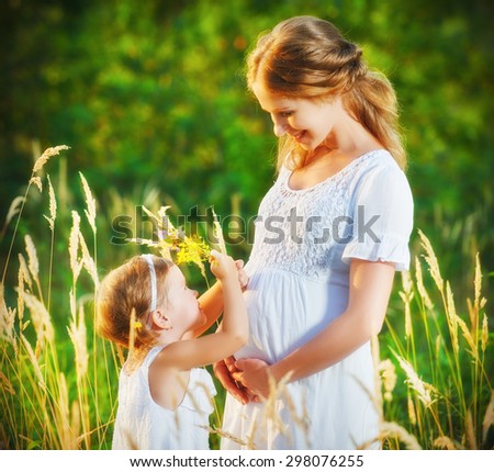 happy family, a pregnant mother and daughter little girl child in the summer  meadow with yellow flowers