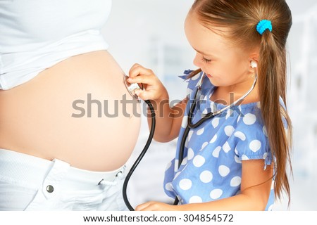 happy family and pregnancy. daughter playing doctor stethoscope and listens to her mother\'s pregnant belly