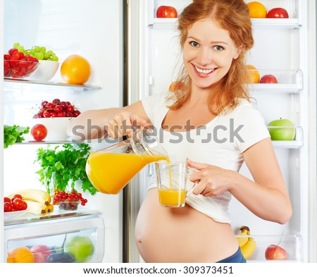 nutrition and diet during pregnancy. Pregnant woman standing near refrigerator with with orange juise