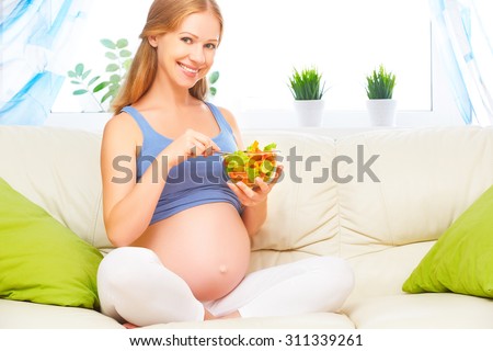 happy pregnant woman eats healthy food vegetable salad on the sofa at home