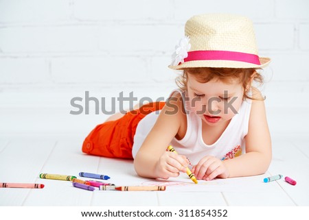happy little artist  girl in a hat draws pencil lying on the floor
