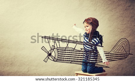Happy baby dreams of becoming a pilot aviator and plays with planes on background wall of house