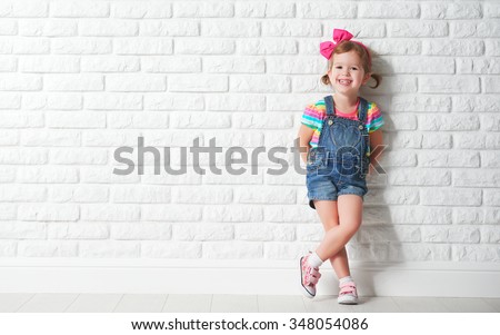 Happy child little girl laughing at a blank empty brick wall