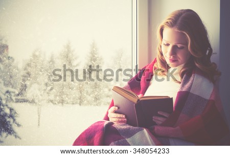 happy girl reading a book by the window in the winter