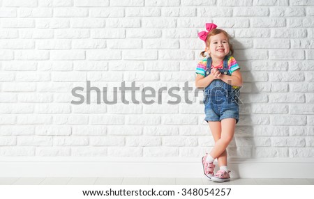 Happy child little girl laughing at a blank empty brick wall