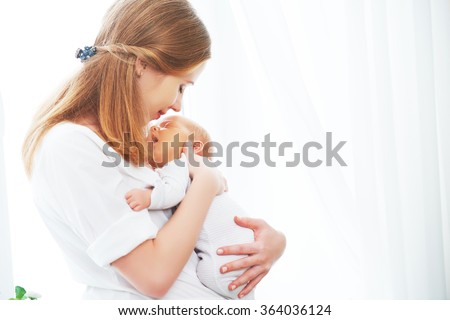 newborn baby in a tender embrace of mother at the window