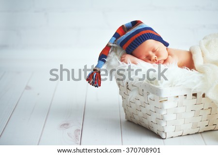 Cute happy newborn baby in a blue knit cap sleeping in a basket