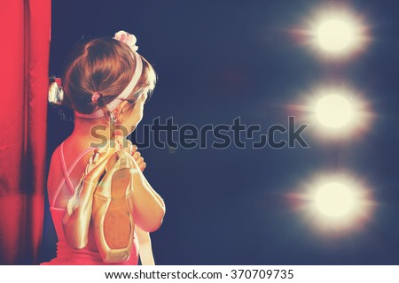 little child girl ballerina ballet dancer on the stage in red side scenes and looking in odeum