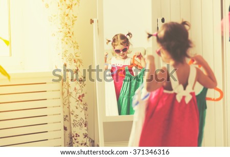 little girl child looks into the mirror and choose dresses