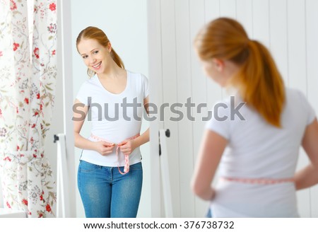 young woman measuring waist with measuring tape in front of a mirror