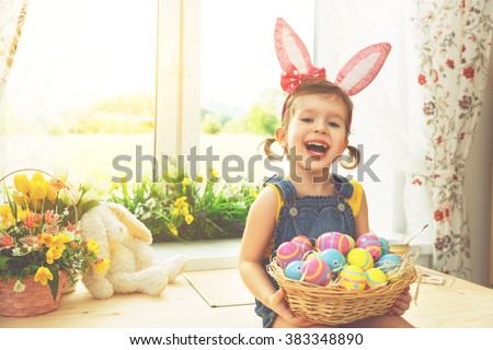 Easter. happy child girl with bunny ears and colorful eggs sitting at the window of a house in flowers