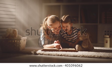 happy family mother and daughter read a book in the evening at home