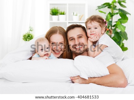 happy family mother, father and two children at home in bed