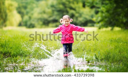 happy child girl running and jumping in puddles after rain in summer