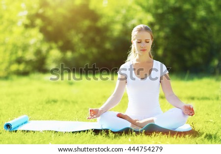 young woman enjoying meditation and yoga on green grass in the summer on nature