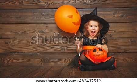 funny child girl in witch costume for Halloween with pumpkin Jack and orange balloon on a dark wooden background