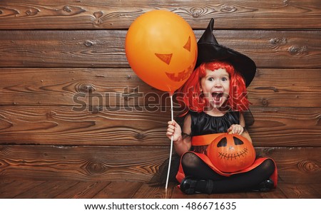 funny child girl in witch costume for Halloween with pumpkin Jack and orange balloon on a dark wooden background