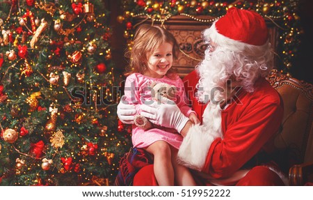 child girl in a nightgown sitting on the lap of Santa Claus around Christmas tree
