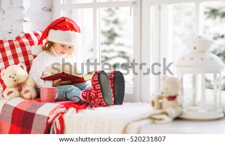 happy child girl reading a book while sitting at a winter window Christmas