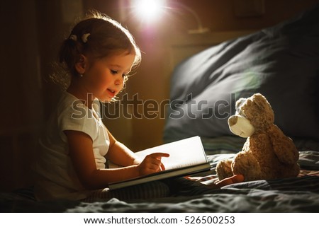 child girl reading a book in bed before going to sleep