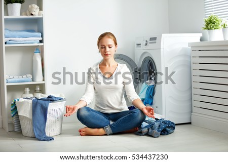 concept. tired housewife meditates in lotus position in laundry room near washing machine and dirty clothes