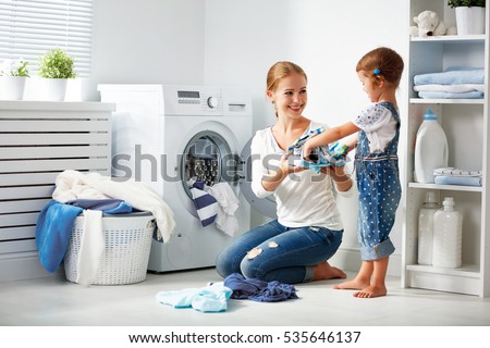 family mother and child girl little helper in laundry room near washing machine and dirty clothes