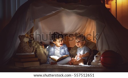 children boy and girl reading book with flashlight in  tent at night
