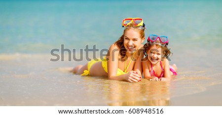 Happy family mother and chid daughter in masks for swimming on the beach in summer