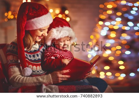 Christmas Eve. family mother and baby reading magic book at home near the fireplace and the Christmas tree