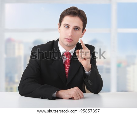 successful business man seriously sitting at a desk in his office and shows the index finger of the hand