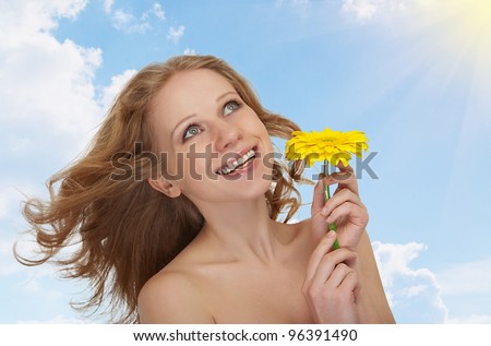 beautiful young woman with flowing hair with a yellow gerbera flower against the sky with clouds and sun