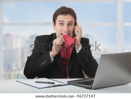 frightened frustrated business man talking on the phone, bites a tie, experiences fear and stress