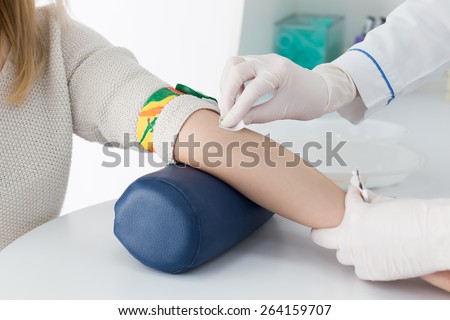 Preparation for blood test with beautiful young blond woman by female doctor in white coat medical uniform on the table in white bright room. Nurse rubbing a hand sterile patient tissue.
