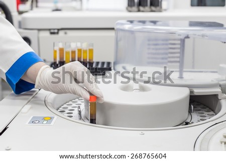 Grey centrifuge to obtain the results of a blood test, with uniformly arranged tubes. Medical worker in white gloves inserts or take the tube from the centrifuge.