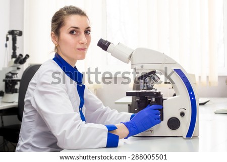 Medical worker women in blue gloves working with microscope in white light and a medical laboratory.