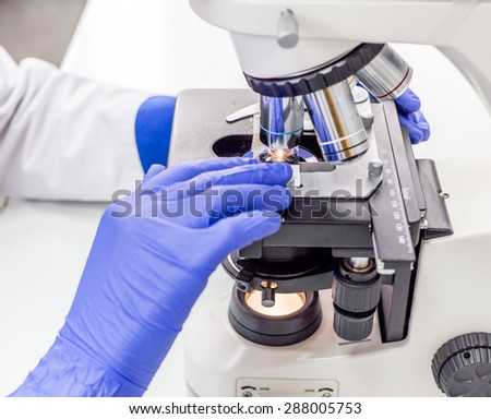 Medical worker in blue gloves working with microscope. Macro photo of lens optical microscope shot close-up in white light and a medical laboratory.