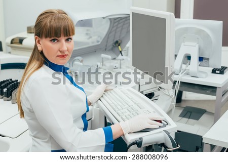 Medical worker woman in white uniform and gloves working in the laboratory on computer in light and clean clinic. Nurse beautiful and smiling.
