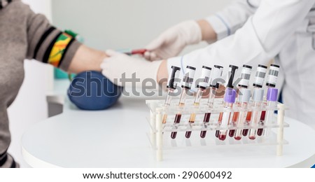 Blood test from vein in arm, pinched wiring,by vacuum system of needle and tube, which is full of red venous blood. Test taking by nurse in white gloves.In front of it stand the test tubes with blood.