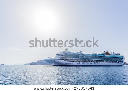Big cruise liner which is more than a mountain in the background goes from port to travel around the world on a bright sunny day. In the picture: sun, blue sea, a big white ship.