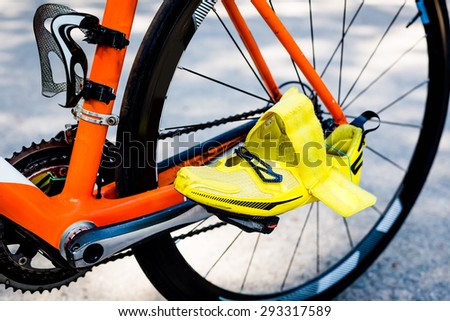 Close-up of black rear wheel of the bicycle, an orange frame, bright yellow cycling shoe in the foreground ready to start cycling stage competitions in a triathlon.