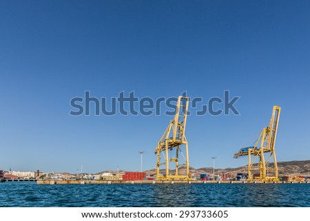 Photo Sea port with a dock, where stands large yellow crane. On the background you can see a lot of blue, red, yellow and gray containers.