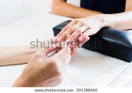 Beautician doing a manicure in a salon attending to a ladies cuticle pushing it back to enhance the nail, close up view of the hands