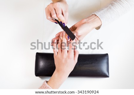 Top view of image of hands polishing fingers on towel clients central finger. Woman in nail salon receiving manicure by beautician.