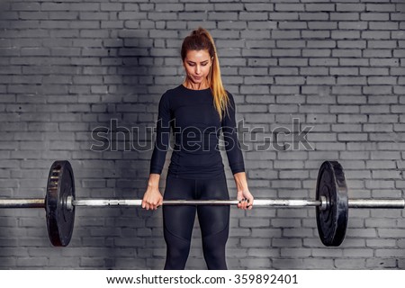 Back view young adult girl doing heavy duty squat in gym with barbell. Woman with perfect abs doing squat exercises. Blonde fit woman in great shape in Fitness