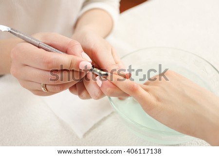 Closeup finger nail care by manicure specialist in beauty salon. Manicurist clear cuticle professional manicure tool.