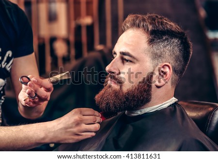 Closeup professional grooming beard with scissors in a Barbershop. Portrait of a bearded man hipster in a Barbershop during haircut. Stylish man hair cut at the barber shop.