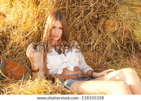 Beauty woman relaxing in the straw in field. Young woman in costume of cowboy looks at camera.
